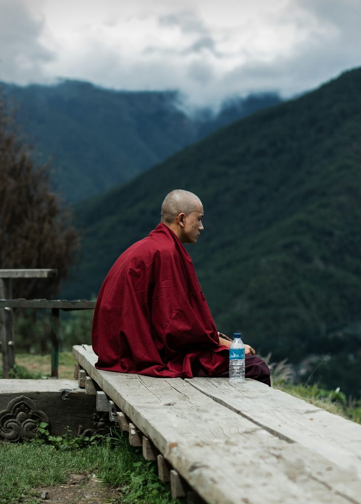 A monk in a red robe looking out over the mountains near Thimphu